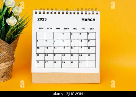 Weißer Kalender März 2023 mit Topfpflanze auf gelbem Hintergrund. Stockfoto