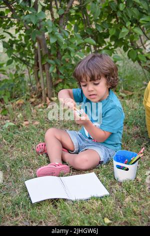 Die Jungen im Grundschulalter lieben es, in Parks zu malen. Jungen zeichnen Bilder als Outdoor-Hobby. Konzept der Bildung außerhalb der Schule. Stockfoto