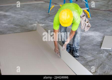 Bauarbeiter/Trockenbauer schneidet ein Trockenbaublech für die sofortige Installation im Inneren eines im Bau befindlichen neuen Mehrfamilienhauses. Stockfoto