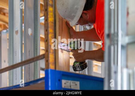 Ein Bauarbeiter installiert ein Stück verzinktem Stahlrahmen an einer vertikalen 2x6-Holzbalken-Strebe in einem Neubau Stockfoto