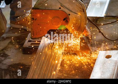 Der Bauarbeiter verwendet eine Metallsäge, um verzinkte Stahlrahmenstreben für die Installation in einem Neubau zu schneiden Stockfoto