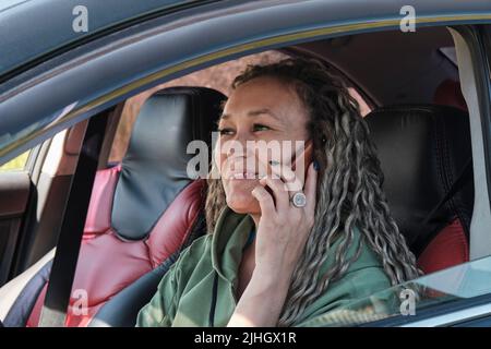 Eine attraktive asiatische lächelnde Frau mittleren Alters, die in einem Auto sitzt und am Telefon telefoniert. Stockfoto