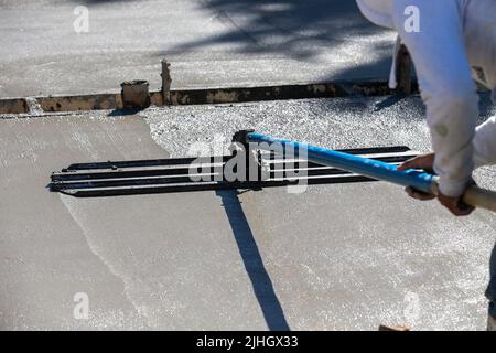 Bauarbeiter mit einem großen abgerundeten Bullfloat-Messer mit langem Griff, um frisch gegossenen Beton eines neuen Hauses im Bau zu glätten Stockfoto