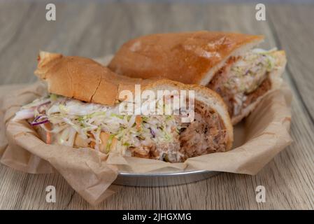 Verführerisches BBQ Pulled Pork Sandwich mit Salat und Gurke auf einem frisch gebackenen italienischen Brötchen serviert. Stockfoto