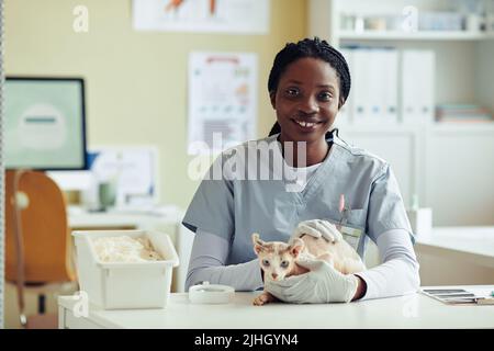 Porträt eines lächelnden jungen Tierarztes am Arbeitsplatz, der mit einer Katze in der Tierarztklinik posiert, Kopierraum Stockfoto