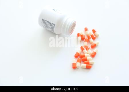 Aus der Medikamentenkiste verschüttete Kapseln auf einem isolierten weißen Hintergrund. Orange und weiße Pillen. Selbstmordgedanken. Vitamine, Nahrungsergänzungsmittel. Niemand. Stockfoto