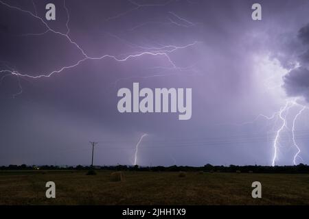 Gewitter über dem Feld mit rollenden Ballen in der Nacht, Blitze in Wolken in der Nacht auf dem Land Stockfoto