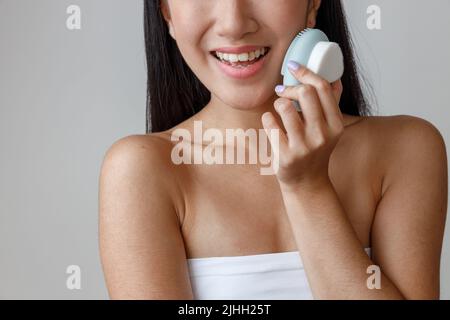 Fröhliche asiatische Frau, die im Studio Gesichtsmassager verwendet Stockfoto
