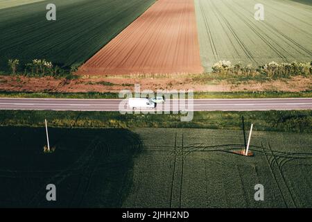 Weißer Lieferwagen und grüner Pkw, die auf der Autobahn durch die Landschaft fahren, Drohne pov aus der Vogelperspektive Stockfoto