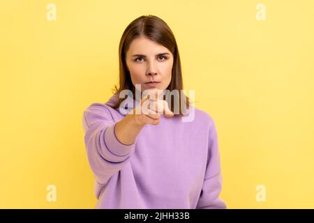 HE, Sei vorsichtig. Junge Erwachsene streng herrisch Frau ernsthaft zeigen Finger und Blick auf die Kamera, Warnung, tragen lila Hoodie. Innenaufnahme des Studios isoliert auf gelbem Hintergrund. Stockfoto