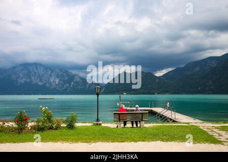 Attersee - berühmter österreichischer türkisfarbener See. Der Blick auf zwei alte Damen, die auf der Holzbank vor dem türkisfarbenen See sitzen. Stockfoto