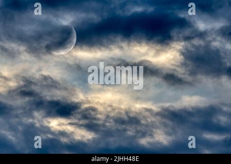 Der Mond steigt inmitten Eines farbenprächtigen, wolkigen Sonnenuntergangshimmels auf Stockfoto