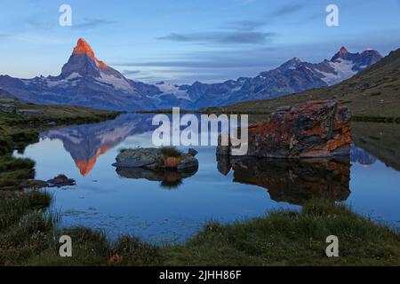 Der Sonnenaufgang beleuchtet den Gipfel des Matterhorns, der auf einem Bergsee reflektiert. Stockfoto