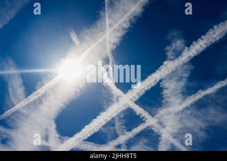 An einem sonnigen Sommertag in Surrey, Südostengland, treten weiße Dampfspuren und Wolken von Flugzeugen des Flughafens Heathrow an einem blauen Himmel auf Stockfoto