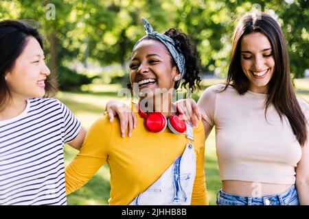 Drei multirassische beste Freundinnen, die gemeinsam im öffentlichen Park lachen Stockfoto