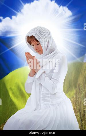 Eine in Weiß gekleidete Frau betet auf dem Hintergrund der ukrainischen Flagge Stockfoto