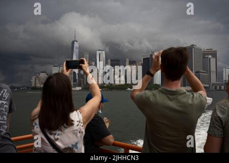 New York, USA. 18. Juli 2022. Die Passagiere der Staten Island Ferry fotografieren dramatische Sturmstürme über dem unteren Manhattan, während Prognostiker diese Woche Temperaturen über 90 Grad Fahrenheit (32 Grad Celsius) vorhersagen Stockfoto