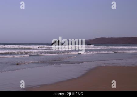 Ein ruhiger, leicht bewölktes Nachmittag an einem Strand in der Nähe von Cayucos, CA mit wenigen Menschen und sanften Wellen. Morro Bay liegt in der Ferne mit seinem riesigen Felsen. Stockfoto