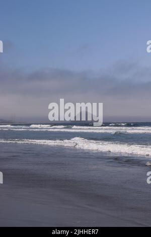 Ein ruhiger, leicht bewölktes Nachmittag an einem Strand in der Nähe von Cayucos, CA mit wenigen Menschen und sanften Wellen. Morro Bay liegt in der Ferne mit seinem riesigen Felsen. Stockfoto