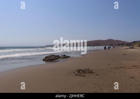 Ein ruhiger, leicht bewölktes Nachmittag an einem Strand in der Nähe von Cayucos, CA mit wenigen Menschen und sanften Wellen. Morro Bay liegt in der Ferne mit seinem riesigen Felsen. Stockfoto