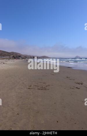 Ein ruhiger, leicht bewölktes Nachmittag an einem Strand in der Nähe von Cayucos, CA mit wenigen Menschen und sanften Wellen. Morro Bay liegt in der Ferne mit seinem riesigen Felsen. Stockfoto