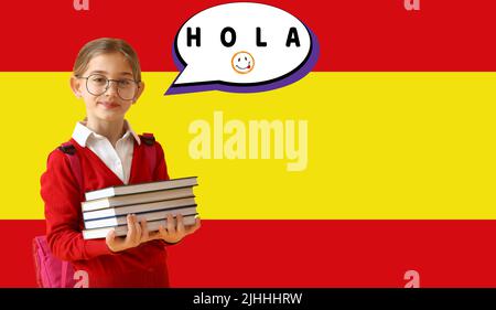 Kleines Schulmädchen mit Büchern und Sprechblase mit Wort HOLA (HALLO) gegen Flagge Spaniens Stockfoto