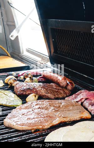 Grill ist von der Seite mit oberen Sirloin geschnitten und gerösteten Nopales zu sehen.Hintergrundbeleuchtung. Würstchen auf dem Grill. Hausgemachter Braten. Mexikanisches Roastbeef. Stockfoto