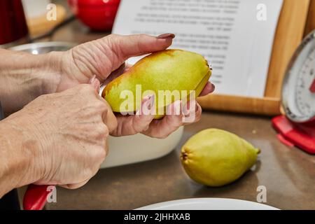 Der Koch schneidet die Birnen in Scheiben für den Schokoladenkuchen mit Birne und Nüssen. Schritt für Schritt Rezept Stockfoto