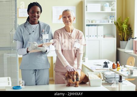 Vorderansicht Porträt von zwei Tierärztinnen, die in der Tierarztklinik die Kamera betrachten, während sie den Hund untersuchen, Kopierraum Stockfoto