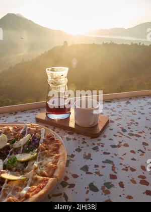 Pizza- und Kaffeefrühstücksmenü, serviert auf dem Tisch mit dem Hintergrund des Sonnenaufgangs Stockfoto