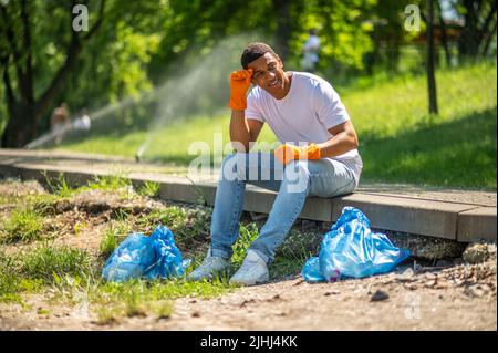 Mann, der in der Nähe von Paketen im Park sitzt Stockfoto