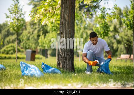 Kerl, der neben dem Baum hockt und Müll abholt Stockfoto