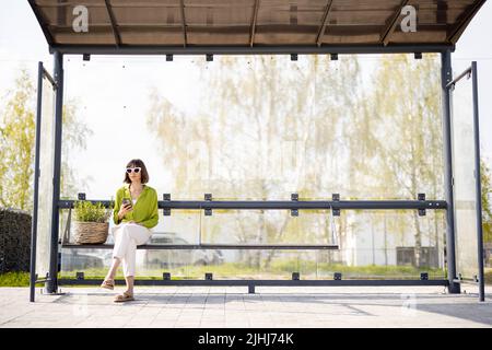 Frau mit Blumentopf an der modernen Bushaltestelle Stockfoto