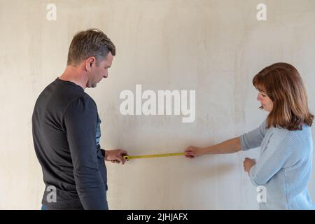 Junges Paar zieht in neue Wohnungen. Die Menschen messen die Größe der Wand mit einem Maßband. Konzept neue Häuser, Neuanfang. Hochwertige Fotos Stockfoto