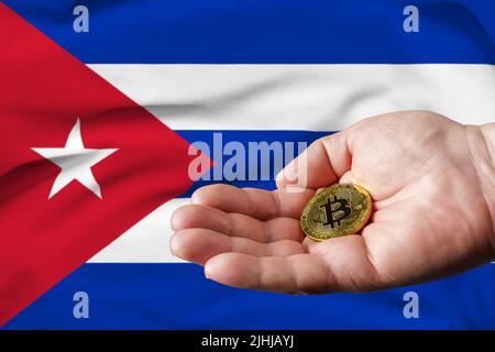 Goldene Bitcoin-Münze in der Hand des Mannes, Kuba-Flagge im Hintergrund. Stockfoto