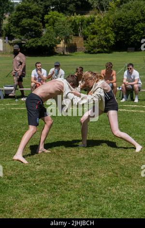 Ein junges Teenager-Mädchen, das mit einem Jungen kämpft, der beim Grand Cornish Wrestling Tournament auf dem malerischen Dorfgrün von St. Mawgan in Pydar i teilhat Stockfoto