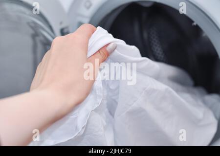 Nahaufnahme von weißer, aufgeräumter Bettwäsche in der Waschmaschine, Haushaltsroutine Stockfoto