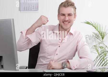 Der Mann hat seine Steuererklärung oder seine Papierarbeit am Schreibtisch gemacht und zeigt eine Siegerpose Stockfoto