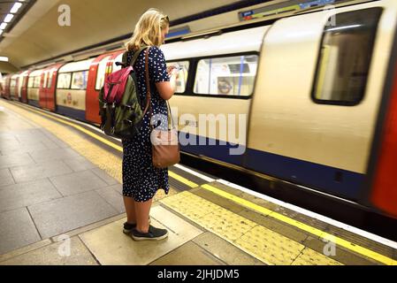 London, England, Großbritannien. London Underground - Frau auf dem Bahnsteig, die ihr Mobiltelefon überprüft Stockfoto