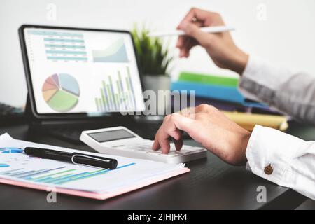 Der junge Geschäftsmann verwendet Rechner und Computer, um die Jahresabschlüsse zu Hause zu überprüfen, anstatt im Büro zu arbeiten Stockfoto