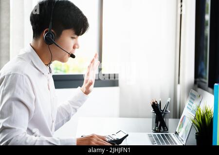 Der junge Geschäftsmann steht auf einer Konferenz mit Menschen, die mit Computern arbeiten, um die Jahresabschlüsse zu Hause zu überprüfen, anstatt im Büro zu arbeiten. Stockfoto