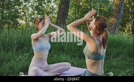 Zwei junge Frauen machen Yoga anjali Mudra im Freien, psychische Gesundheit Stockfoto