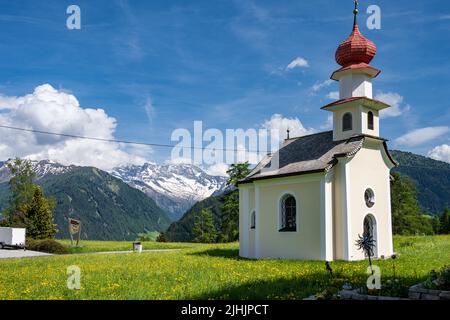 Eine kleine Kapelle auf einer grünen Wiese am Straßenrand einer Landstraße in den Alpen im Sommer Stockfoto