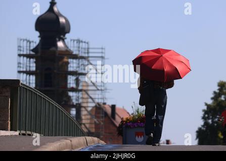 Kitzingen, Deutschland. 19.. Juli 2022. Ein Mann geht mit einem roten Sonnenschirm über die Alte Hauptbrücke. Kitzingen hält seit 2015 den bayerischen Temperaturrekord. Quelle: Karl-Josef Hildenbrand/dpa/Alamy Live News Stockfoto