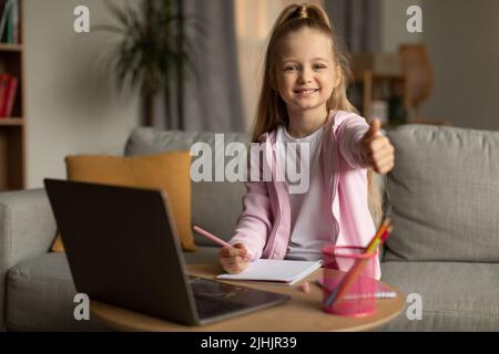 Schulmädchen Bei Laptop Gesturing Thumbs Bis Zu Kamera Zu Hause Stockfoto