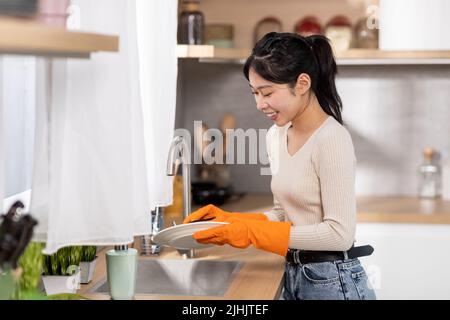 Fröhliche asiatische Frau, die zu Hause Geschirr wäscht Stockfoto