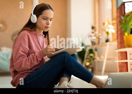 Intelligente fokussierte Schülerin mit Bildungsmaterialien, Büchern und Laptop, die zu Hause an einem Schulprojekt arbeitet Stockfoto