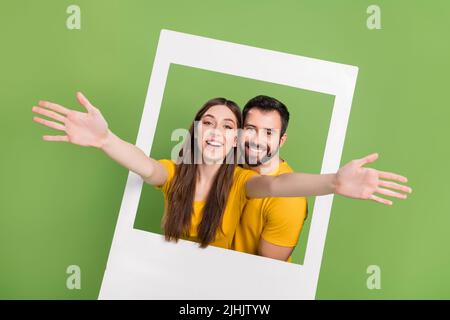 Porträt von zwei aufgeregten positiven Menschen heben die Arme durch Papierfenster isoliert auf grünem Hintergrund Stockfoto