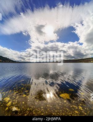 Seenlandschaft mit Felsen unter transparentem Wasser und großen Wolken, die in den Himmel mit Reflexen im Wasser verblassen. Madrid. Stockfoto