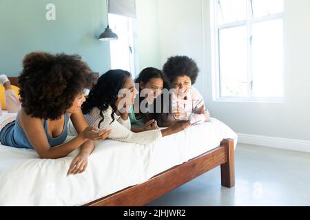 Fröhliche, unbeschwerte biracial junge Freundinnen mit Handy und lachen, während sie auf dem Bett liegen Stockfoto